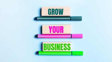 On a light blue background, there are three multi-colored felt-tip pens and wooden blocks with the...