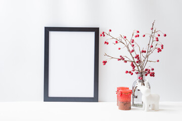 Christmas home interior with decor elements. Mockup with a black frame, branches with red berries...
