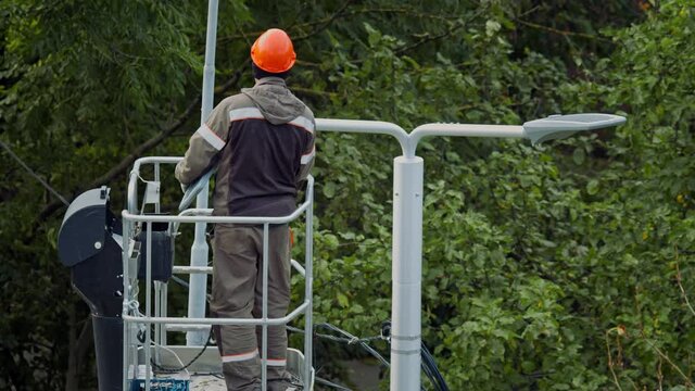 Electrician installs a street light on a pole. Unrecognizable electric utility worker in a boom crane basket installs a new street light instead of old one