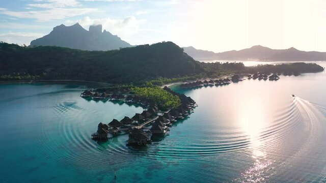 Travel vacation aerial drone video of luxury overwater bungalows resort in coral reef lagoon ocean by beach. Sunset at paradise getaway Bora Bora, French Polynesia, Tahiti, South Pacific Ocean