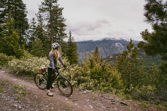 Woman bikes on rocky mountain trail and stops to enjoy view