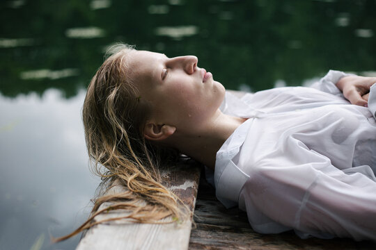 Blonde teenage girl in white shirt with wet hair lying by the pond