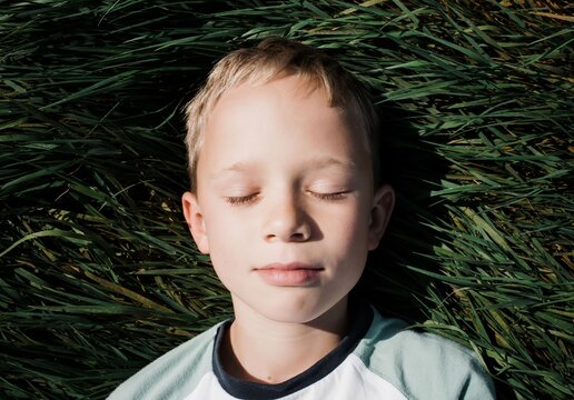 boy lying down in green grass relaxing in the summer sunshine
