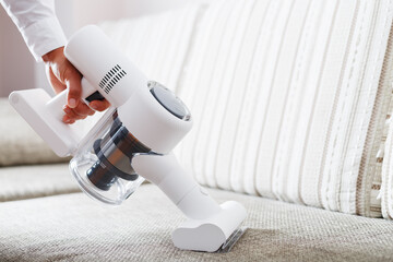 A cordless vacuum cleaner cleans the carpet in the living room with the bottom of the legs. Modern...