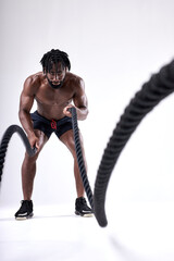 Confident young african american man doing cross fit exercises with ropes over isolated white background. hard workout. wave. shirtless fit athlete guy is concentrated on workout, sport. portrait