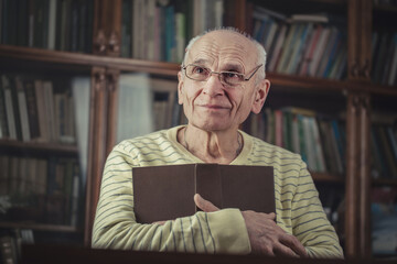 Male aged person in eyewear holds book in hands and looks up with hope. Oldness and human feelings...