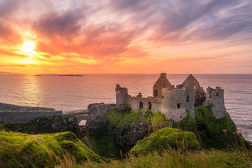 Sunset at ruins of Dunluce Castle located on the edge of cliff, Bushmills, Northern Ireland. Filming location of popular TV show Game of Thrones - obrazy, fototapety, plakaty