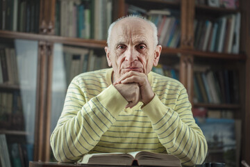 Senior male author sitting at table with book and holds hands under head. Knowledge and education...