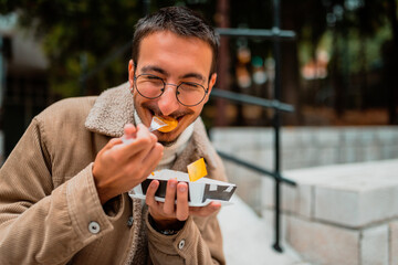 Fototapeta premium A modern guy who wears glasses, sitting in the park and eats fresh poffertjes