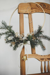 Modern christmas wreath with bell hanging on rustic wooden chair. Winter holidays preparation,...