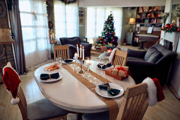 Table setting with lighted candles on decorated Christmas dining table at home.