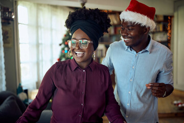 Cheerful black couple dances while celebrating Christmas at home.