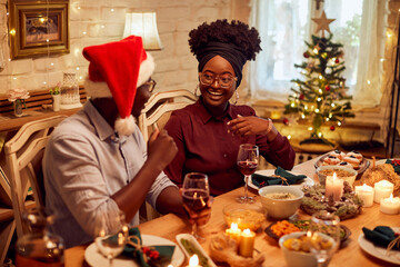 Happy African American couple talks during Christmas lunch at dining table.