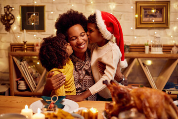 Affectionate black kids kiss their mother at dining table during Christmas meal.