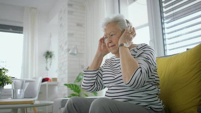 Senior woman at home with smartphone and headphones listening to music.