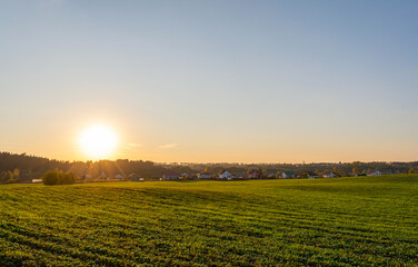 Fototapeta na wymiar Green agricultural field, holiday village on the horizon. Blue orange sky during sunset. Autumn Nature