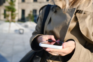Woman is holding a modern smartphone, sending a text message or using an app on her mobile phone. Internet technology user. Smartphone close-up. Focus on the phone screen