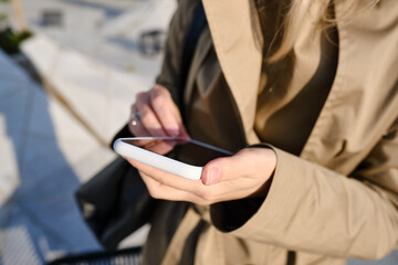 A girl with a smartphone in her hands is standing near the business center. Businesswoman sends a text message or uses an application on her mobile phone. Smartphone close up