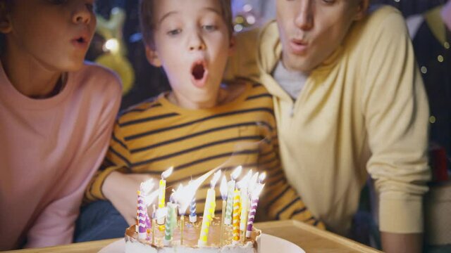 Cute sister and brother with father blow burning candles on delicious birthday cake celebrating family holiday on blurred background close view