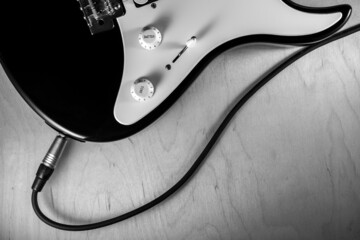 Black and white picture of eletric guitar and cable  on wooden background.