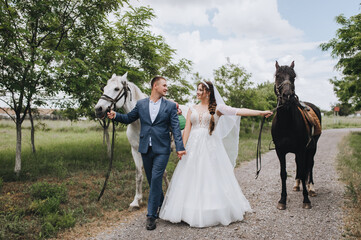 Stylish groom in a blue suit and a beautiful bride in a white long dress walk holding hands in a...