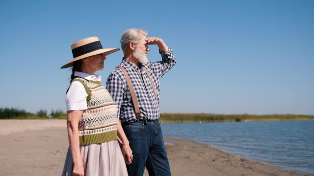 Happy elderly retirement couple resting together by the sea or ocean, beautiful romantic elderly middle-aged grandparents on a sunny summer day