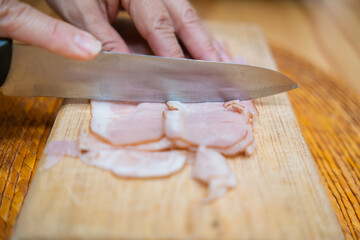 Hands chopping fresh turkey ham slices on a cutting board