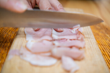 Hands chopping fresh turkey ham slices on a cutting board