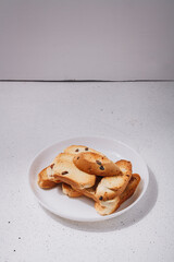 Wheat bread rusks, crackers, sweet croutons with raisins on white plate, wooden background. Tasty homemade appetizer. Copy space, vertical shot