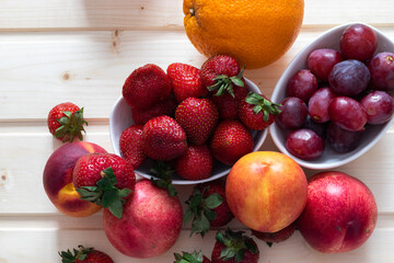 Health and life benefits of strawberries, grapes, nectarines, oranges; high angle photo of fruit on traditional wooden background