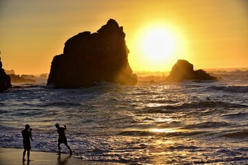 Portugalia. Plaża, Praia da Ursa z sylwetkami fotografujących się chłopców na tle zachodzącego nad oceanem słońca i skał.