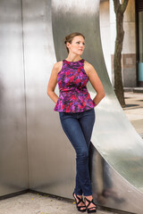 Obraz premium Dressing in a purple pattern top and blue jeans, a young pretty woman is standing by a silver metal structure and waiting for you..