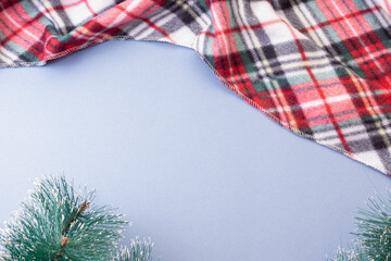 Red plaid and spruce branches on blue background. Space for text. Christmas frame
