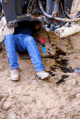 Mechanic working underneath a backhoe leaking oil