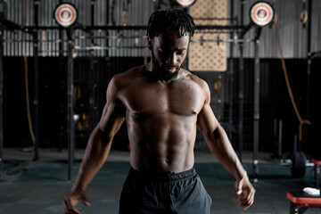 Fototapeta na wymiar atthlete healthy african american man stretching shoulder before gym workout. Fitness strong sportsman with naked torso. Young black shirtless male fit exercising. In dark modern cross fit gym
