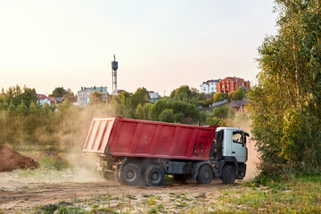 Red dump truck simultaneously lifted the bodies to unload the sand. Cargo transportation services. Large multi-ton truck. Unloading cargo. Construction site and machinery. Banner. Common view