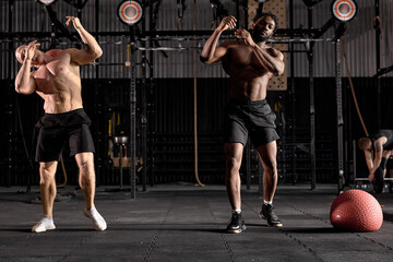 Fototapeta na wymiar two diverse Muscular athletic men exercise with medicine ball at health club or gym. Fitness routine with exercise ball to maintain the abs. Sport, exercising, training and lifestyle concept.