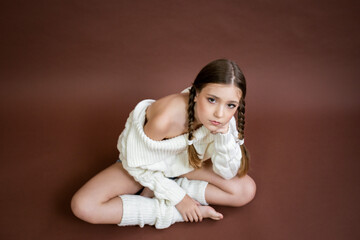 a girl with two pigtails is wearing a white sweater to sit on the floor barefoot