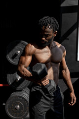 Fototapeta na wymiar active strong sweaty focused fit muscular man with big muscles holding heavy dumbbell for cross fit training, black man do hard core workout in dark modern gym, real people exercising. portrait