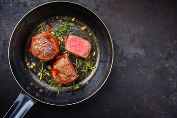 Traditional fried dry aged angus beef filet medaillons natural wrapped with bacon and served as top view in a classic skillet with copy space right