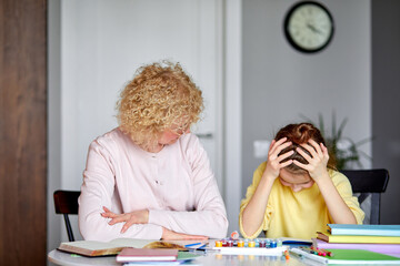 Caring beautiful grandma sit with upset daughter while doing homework, drawing. senior woman helping little girl with homework, support, talk how to solve problem. little girl sit with head bowed