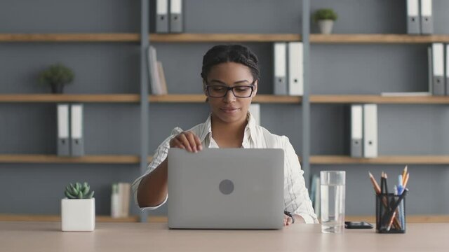 Young cheerful female african american office manager typing on laptop, finishing work and closing computer