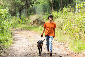 young man wearing an orange t-shirt, walking in the forest with his black dog - Powered by Adobe