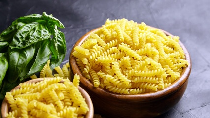Girandole pasta in wooden bowl and green basil herb on black table