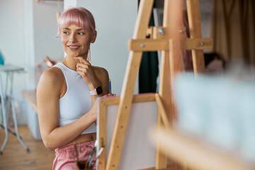 Elegant woman artist sits by easel with blank white canvas on at home