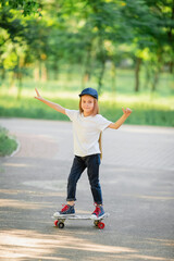Child girl in white T-shirt and jeans is riding skateboard in park and smiling. Happy child. Children's clothing magazine advertising concept