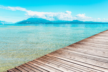 Planked wooden walkway over a tranquil lake with high mountains in the background in a tranquil scene at Lago di Garda.