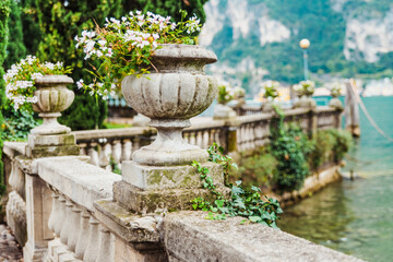 Elegant flower pots decorate the classic stone railing on a romantic walk by a lake in Riva del...