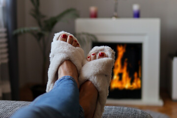 A woman lies cozy bed and relaxing and warming legs on the fireplace at home on winter