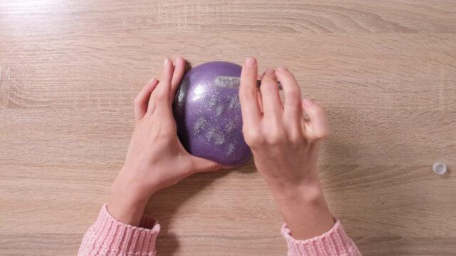 Slime DIY. Female Hands sprinkle glitter on the slime. 4k resolution video. Close up and top view of female hand holding purple shining slime and squeezing it